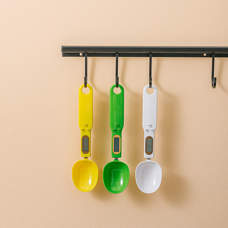 LCD Digital Spoon Scale UK in yellow, green, and white hanging on a rack, perfect for precise cooking measurements.